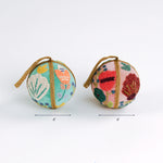 Two decorative beaded Christmas ball ornaments, one in teal and one in pink, each measuring 4 inches wide.