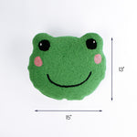 Green frog face pillow with pink cheeks and a smiling expression shown with 15 inch width and 13 inch height.