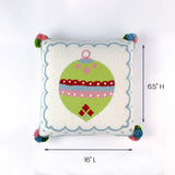 Square white pillow with a green Christmas ornament design and colorful corner pom poms shown with 16 inch length and 6.5 inch height.