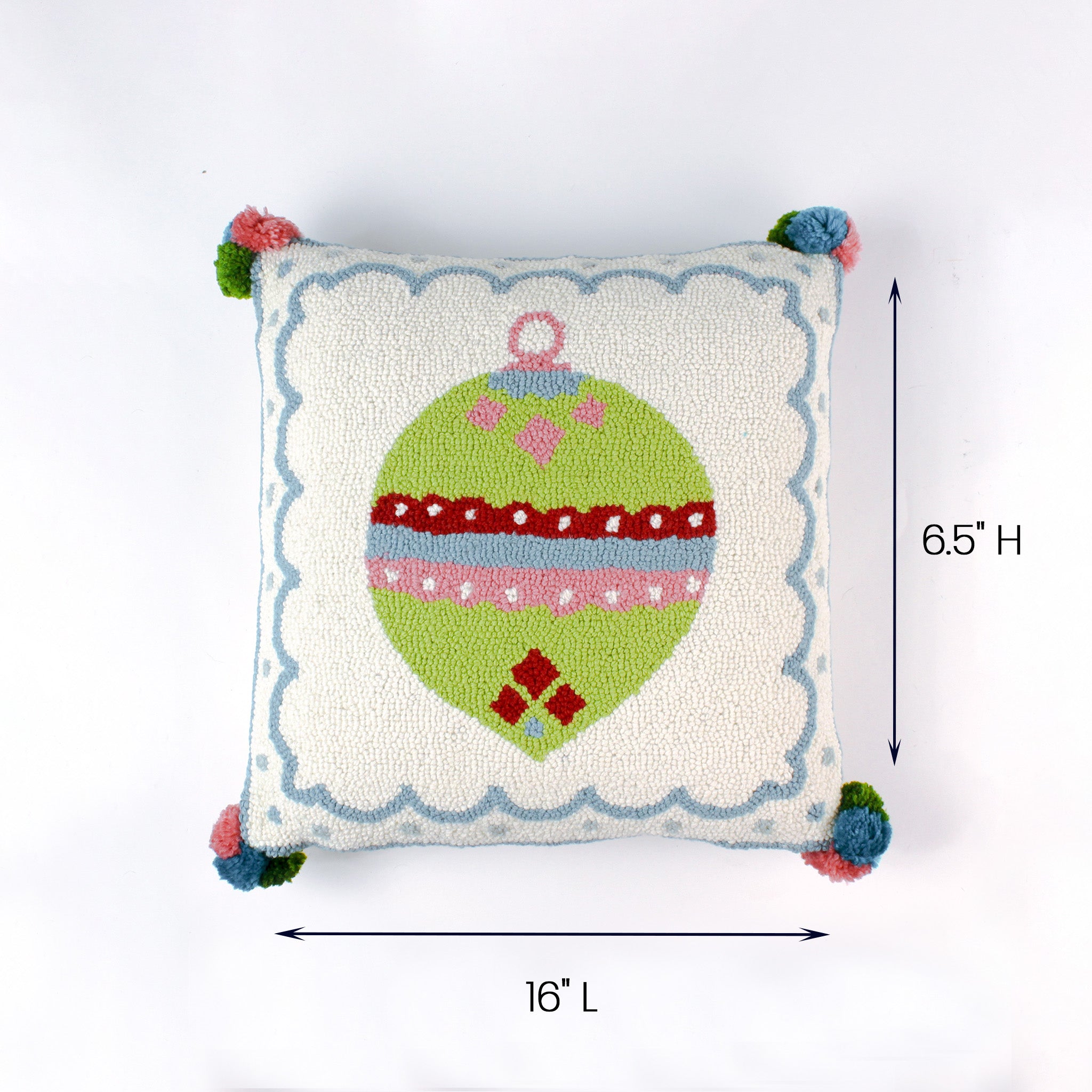 Square white pillow with a green Christmas ornament design and colorful corner pom poms shown with 16 inch length and 6.5 inch height.