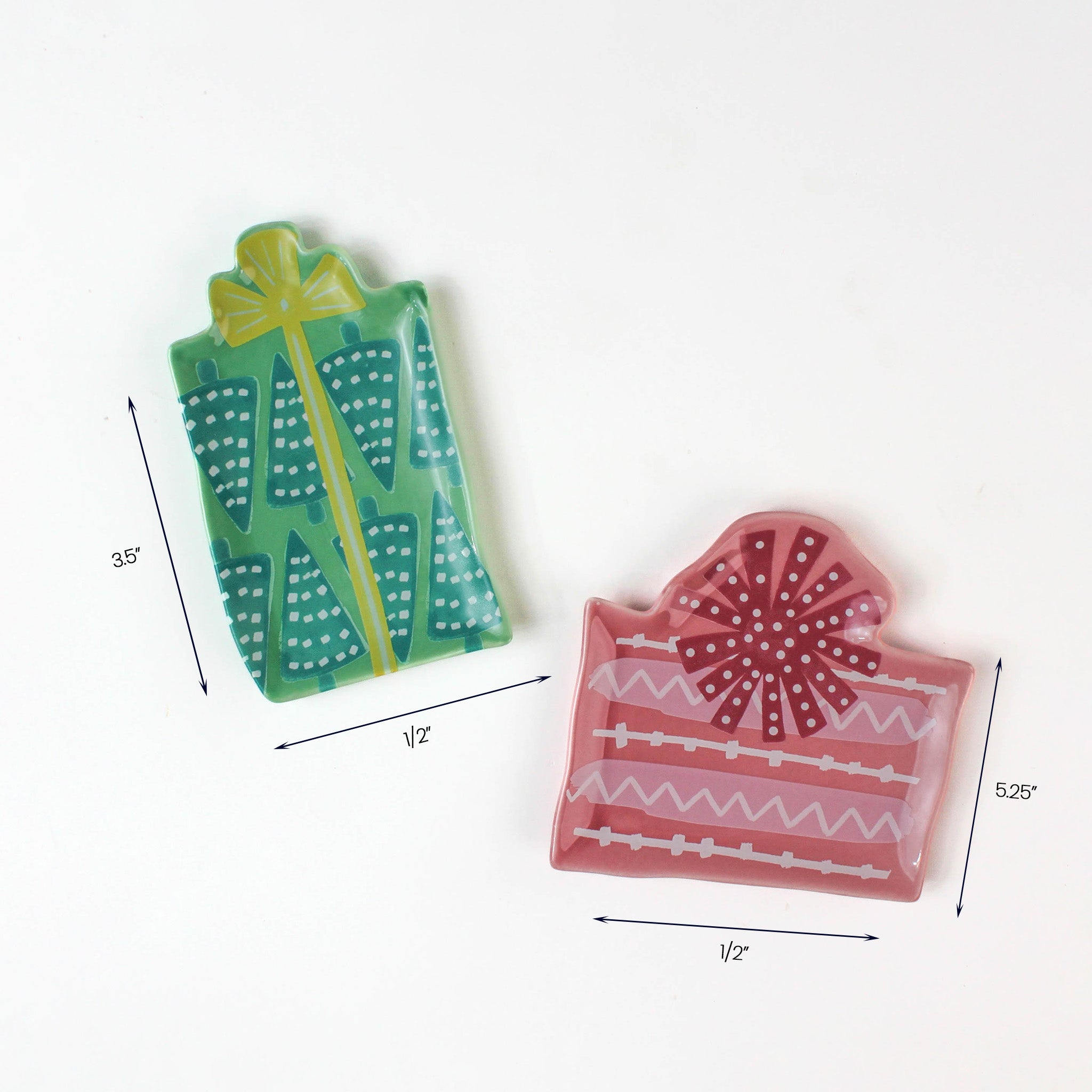 Two small ceramic plates shaped like gift boxes, one green with teal tree patterns and one pink with red ribbon designs, shown with dimensions around 3.5"–5.25" wide.