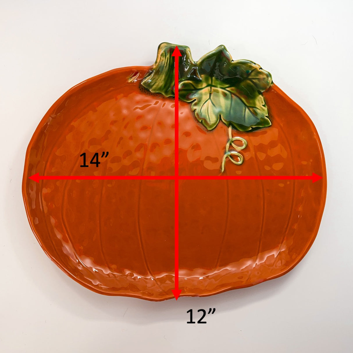 a ceramic pumpkin serving platter with red arrows denoting the dimensions 14" high and 12" across