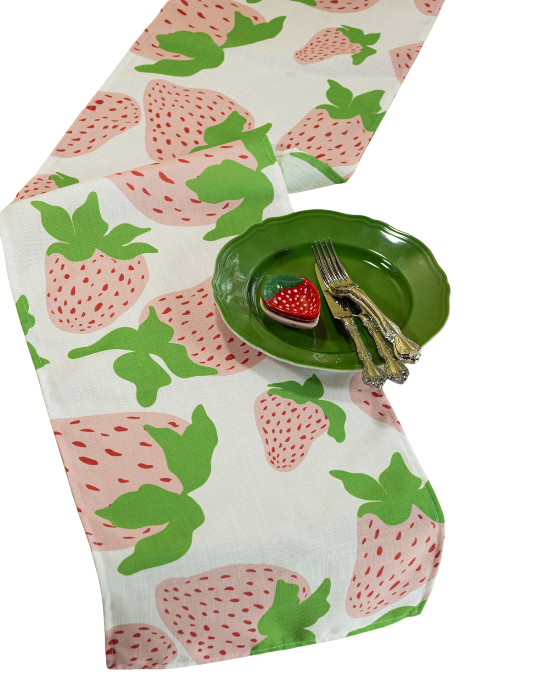 a strawberry fabric table runner designed by madcap cottage with motifs of large pink and green strawberries with green stem and a green plate resting on top.