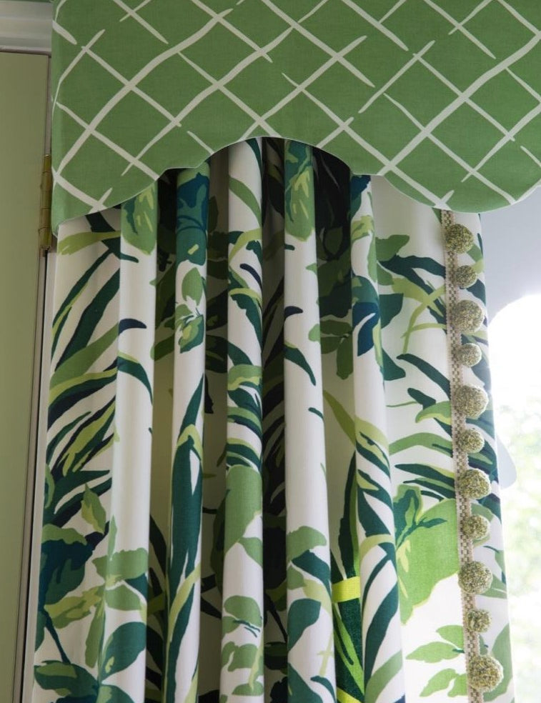 Green tropical leaf patterned drapery panels with matching scalloped valance featuring white lattice design and decorative pom trim.