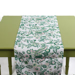 White table runner with green and pink floral pattern displayed on a green table.
