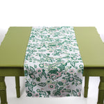 White table runner with green and pink floral pattern displayed on a green table.