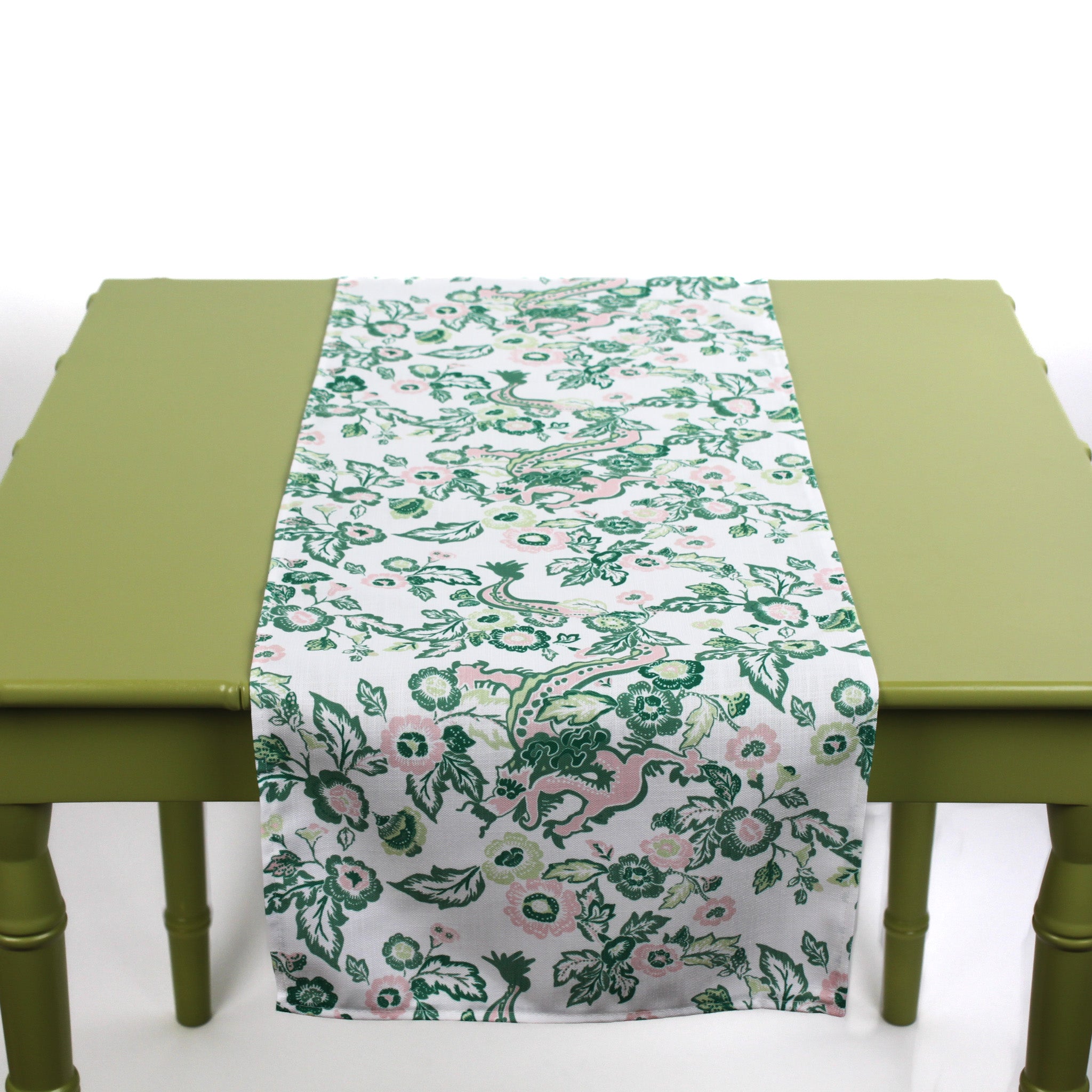 White table runner with green and pink floral pattern displayed on a green table.