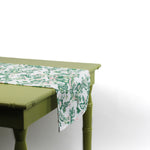 Side view of a white floral table runner hanging over the edge of a green table.