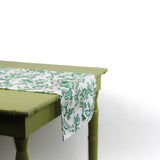 Side view of a white floral table runner hanging over the edge of a green table.