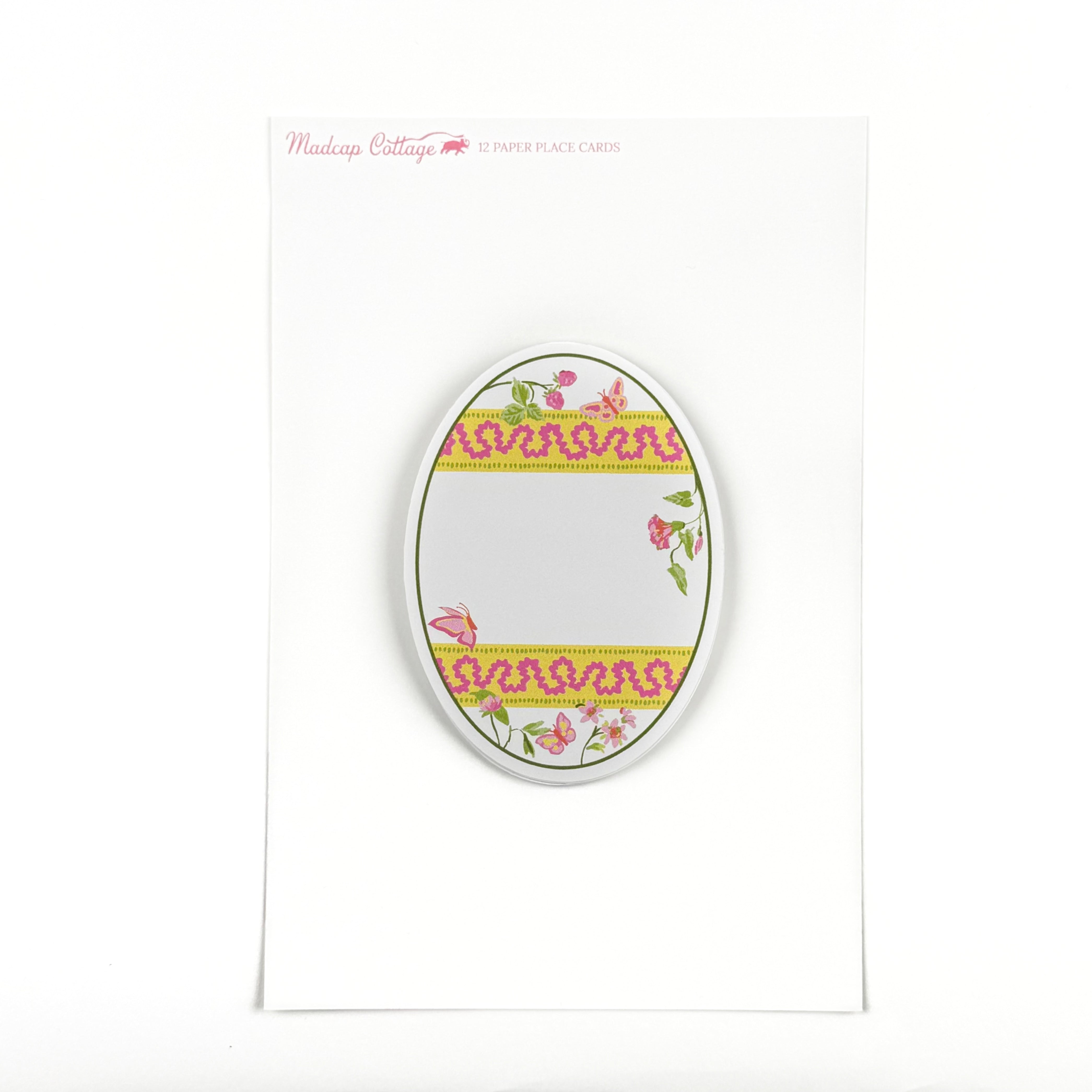 an egg-shaped spring paper place card with a floral and ribbon design on a white background and a pink logo that says Madcap Cottage in the top left corner. 