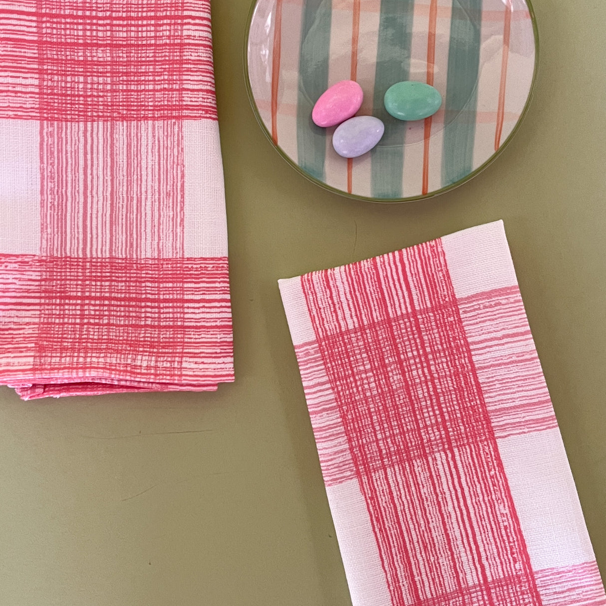two pink gingham dinner napkins in gin lane print fabric by madap cottage next to a plate with small colored easter eggs