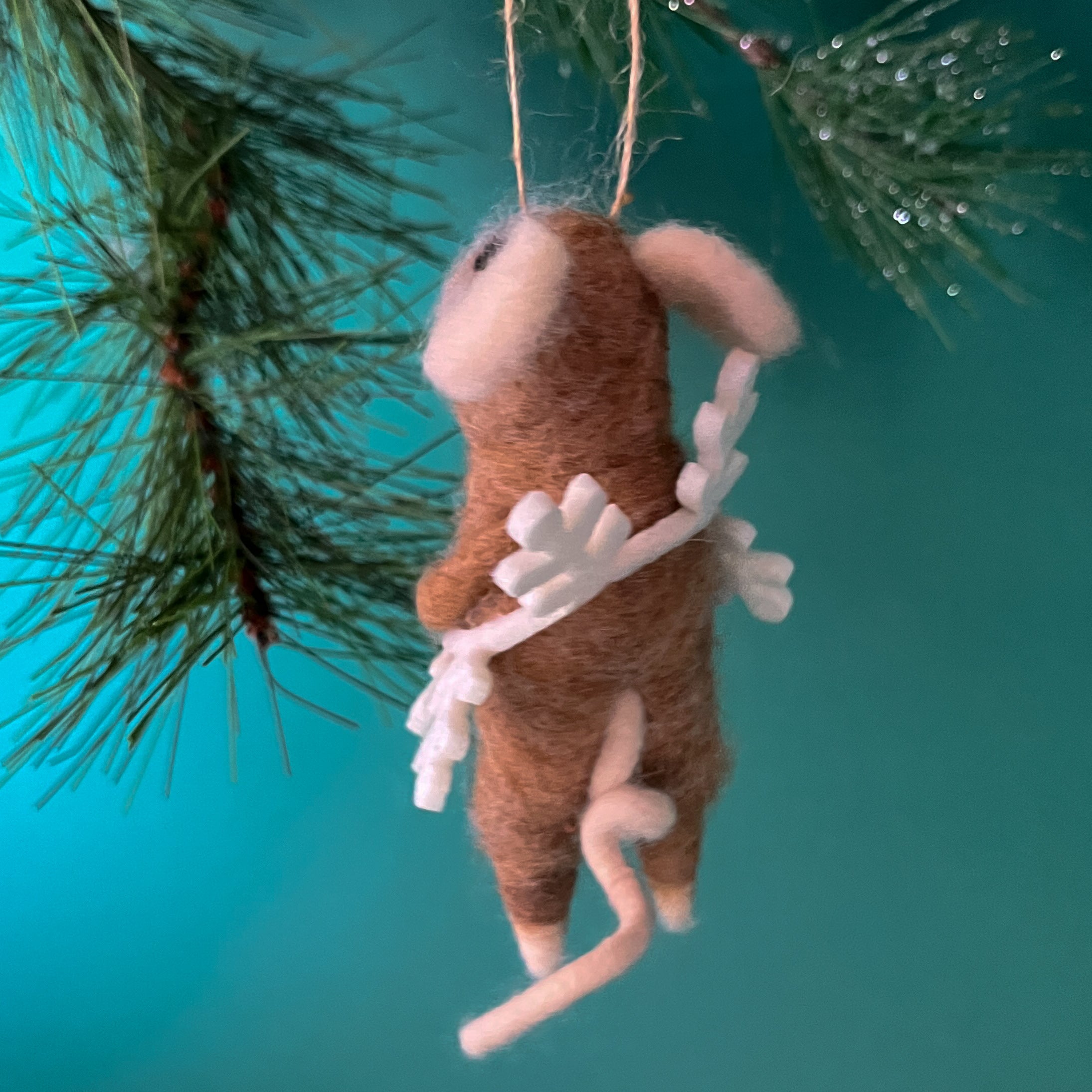 back of one felt mouse ornaments wearing white snowflake costume frame hanging from pine branches