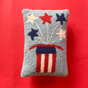 a 4th of july pillow with a striped hat with stars coming out of it. 