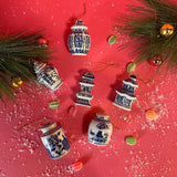Decorative miniature ginger jar ornaments with blue patterns on a red surface with greenery and small ornaments.