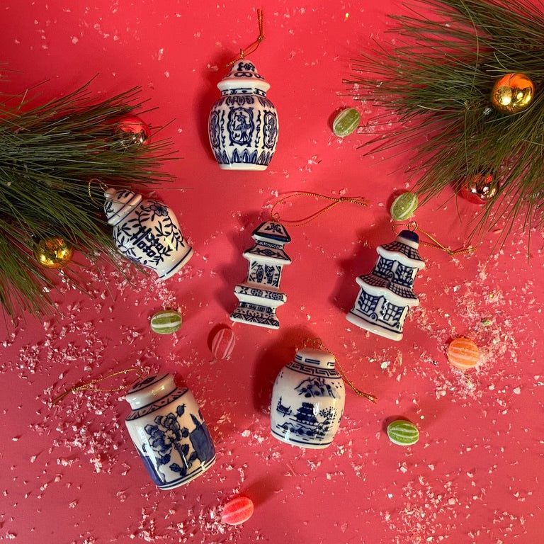 Decorative miniature ginger jar ornaments with blue patterns on a red surface with greenery and small ornaments.