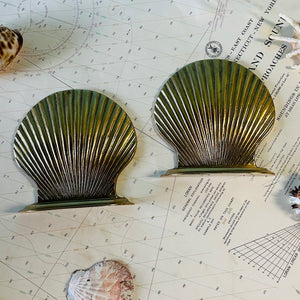 two brass shell bookends lying flat on a marine map, surrounded by shells. 