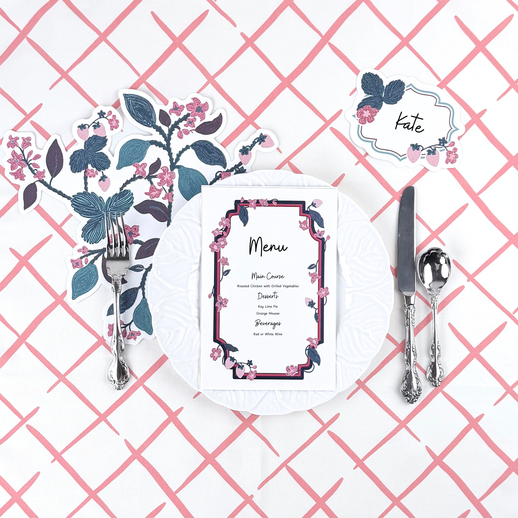 A floral strawberry themed table setting featuring a menu card, decorative napkin, place card, and silverware on a pink crosshatch table runner.