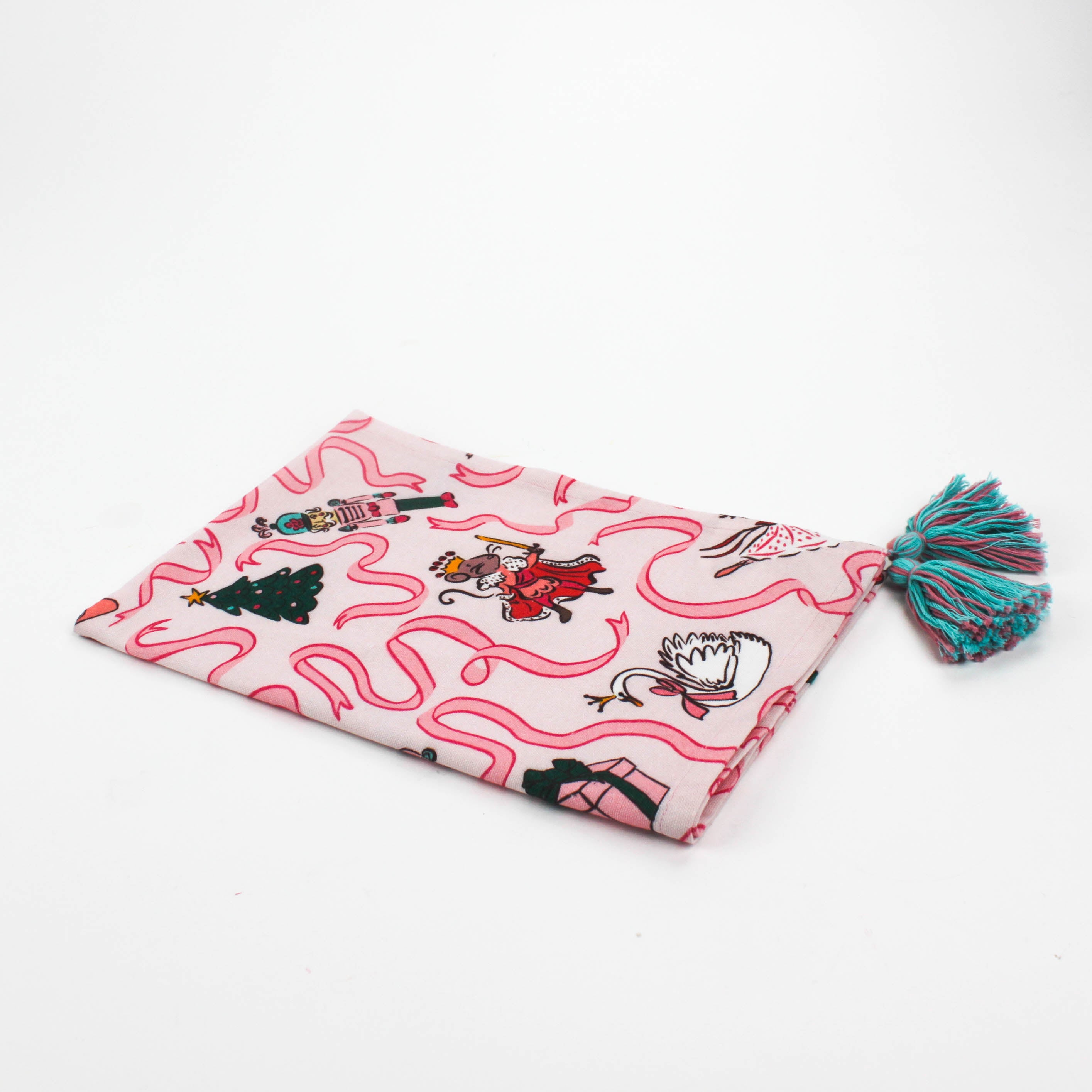 Pink Christmas tea towel featuring Nutcracker-themed illustrations with ribbons, ballerinas, swans, Christmas trees, and presents, finished with teal tassels on each corner.