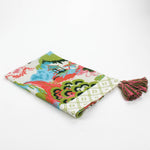 Folded Christmas tea towel featuring a colorful chinoiserie-inspired landscape print with green, pink, and blue tones, finished with a pink and green tassel accent.
