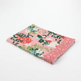 Folded Christmas tea towel with a pink background featuring a floral chinoiserie design and decorative pug dogs among green and red vases, bordered with a geometric pattern.
