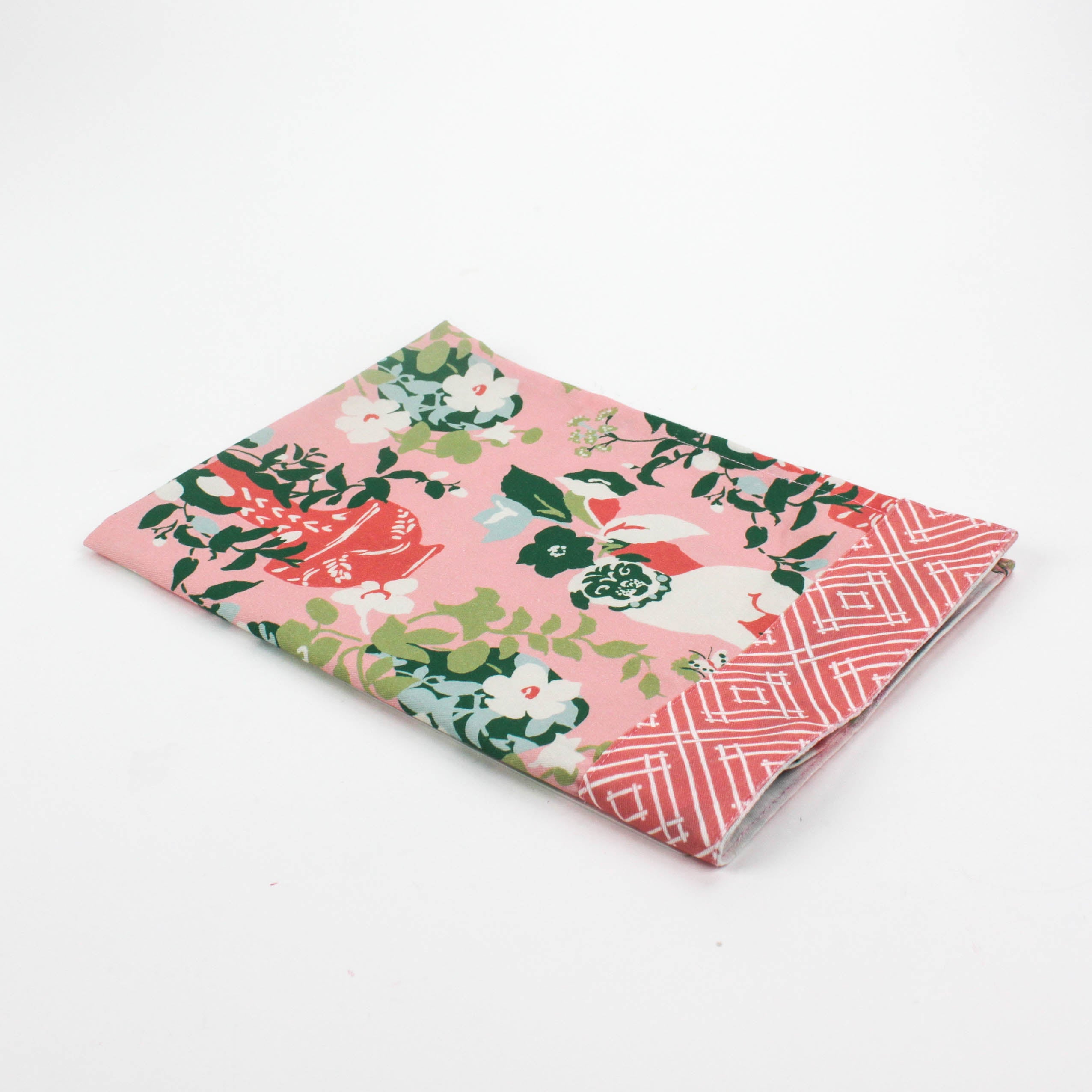 Folded Christmas tea towel with a pink background featuring a floral chinoiserie design and decorative pug dogs among green and red vases, bordered with a geometric pattern.