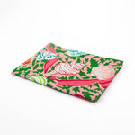Folded Christmas tea towel featuring a pink background with colorful seashell and ribbon patterns accented by green holly-like leaves for a festive coastal look.