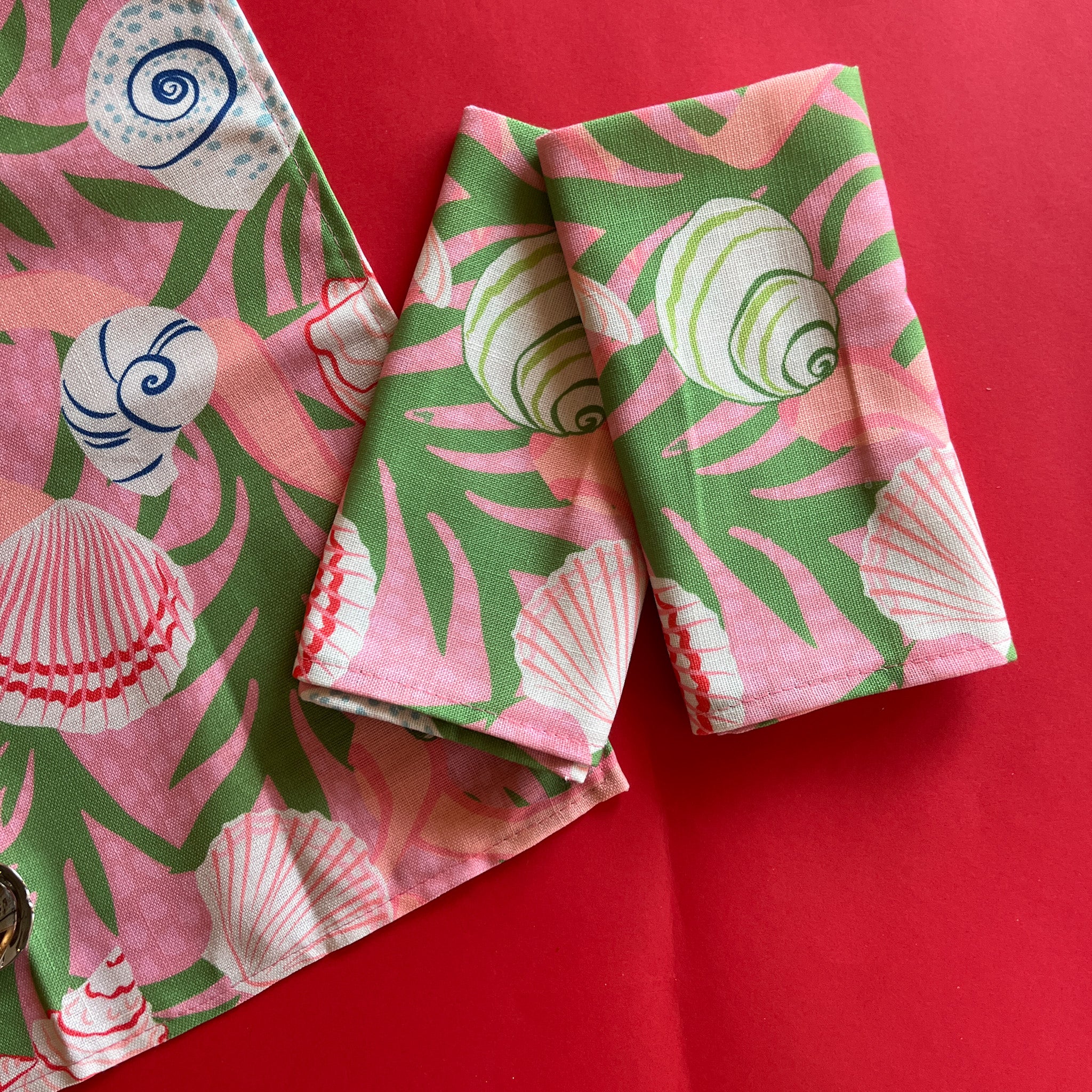 folded pink and green napkins with a shell and seaweed pattern