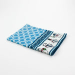 Folded Christmas tea towel featuring a blue lattice pattern with a festive border of cheerful snowmen wearing scarves, hats, and ties in various holiday poses.