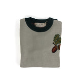Folded neutral knit sweater with embroidered acorn and oak leaf motif and visible branded label