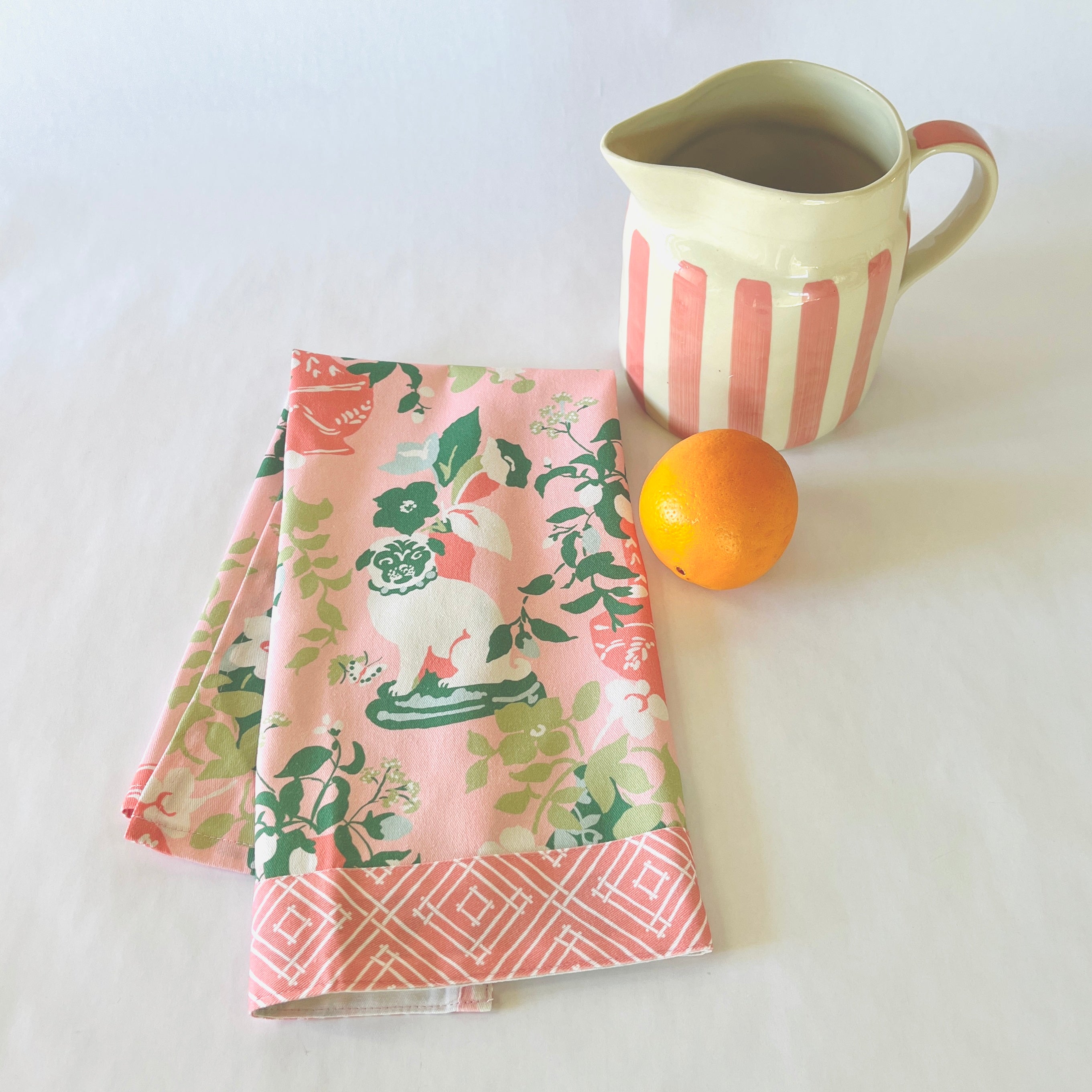 a folded pink chinoiserie tea towel from madcap cottage with pug and vase motifs.