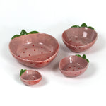 a set of four pink ceramic strawberry dishes in graduating sizes.