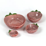 a set of four pink ceramic strawberry dishes in graduating sizes.