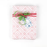 Gift box wrapped in red and white geometric patterned paper with green and red ribbon and a decorative gift tag.