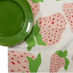 a Garden Party Strawberry cloth table runner designed by madcap cottage with motifs of large pink and green strawberries with green stem and a green plate resting on top