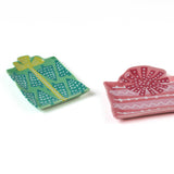 a set of two christmas gift shaped accent plates one in pink and the other in green against a plain white background. 