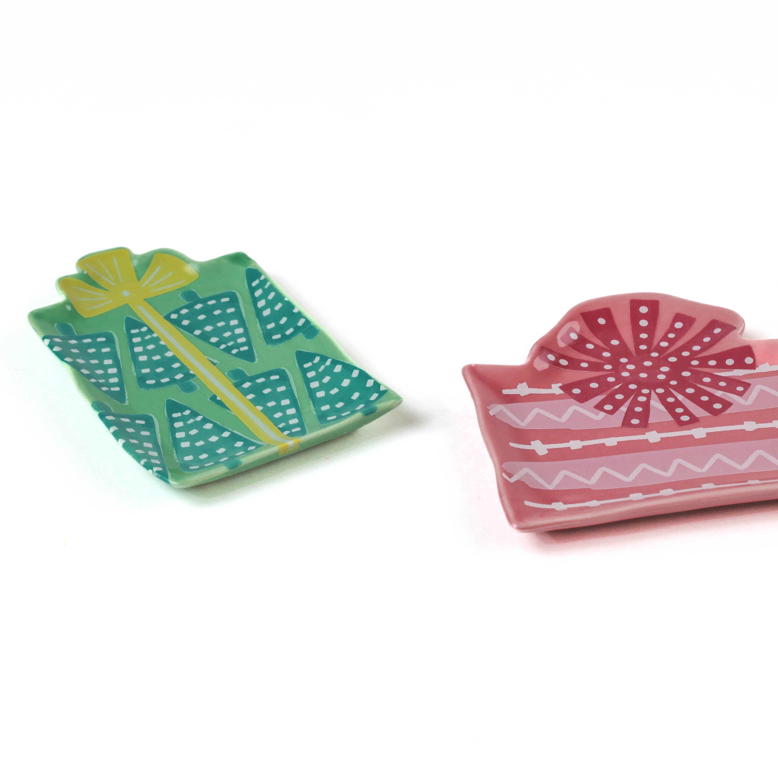 a set of two christmas gift shaped accent plates one in pink and the other in green against a plain white background. 