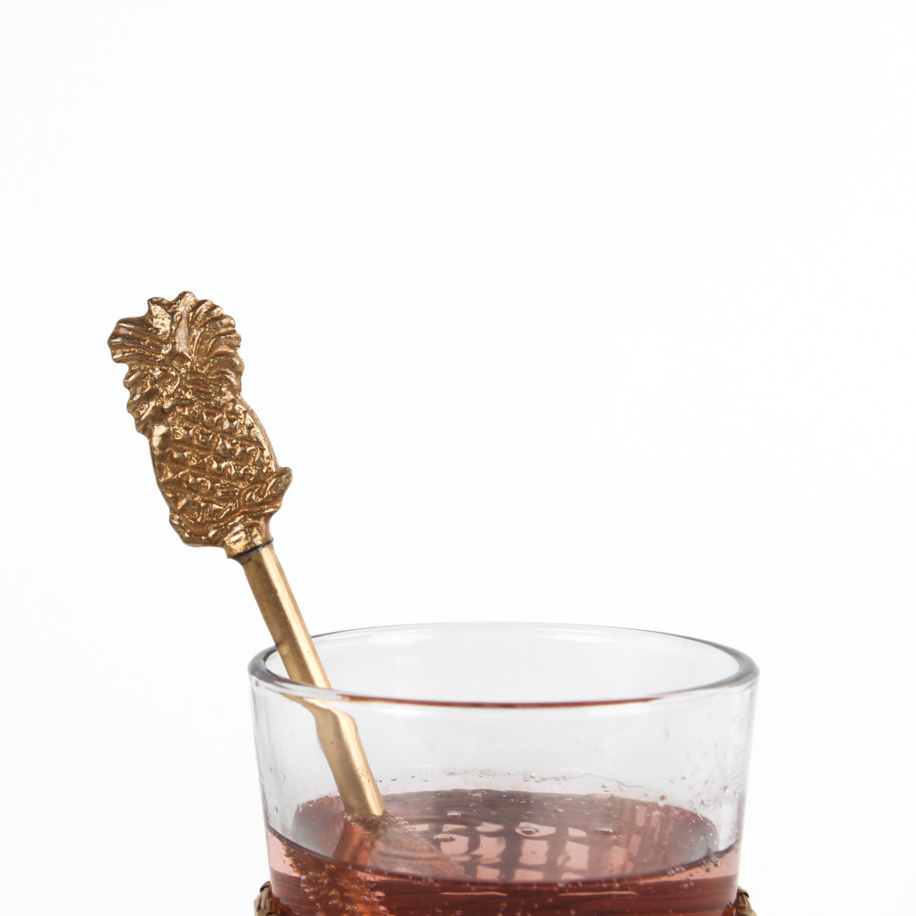 a close up look of a gold pineapple-shaped drink stirrer on a white background