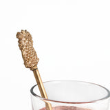 a close up look of a gold pineapple-shaped drink stirrer on a white background