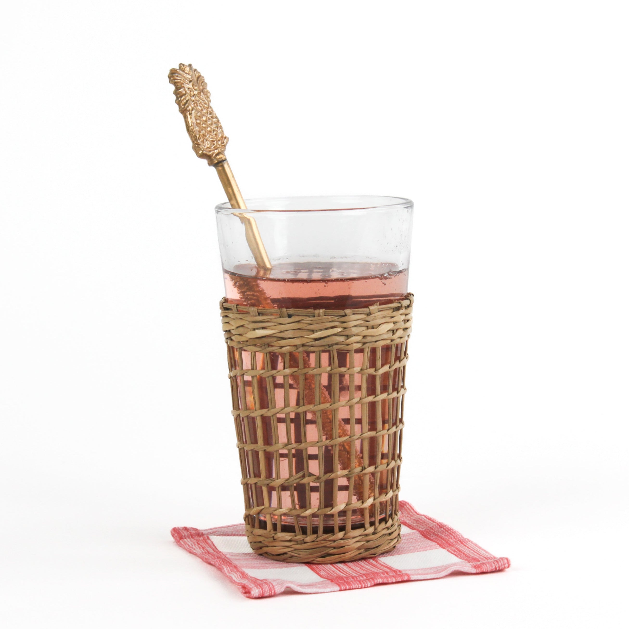 a gold pineapple-shaped drink stirrer on a glass of water on a white background