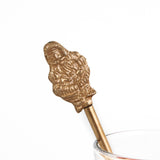 a close up of gilt metal gold christmas swizzle stick with decorative santa ends on a white background
