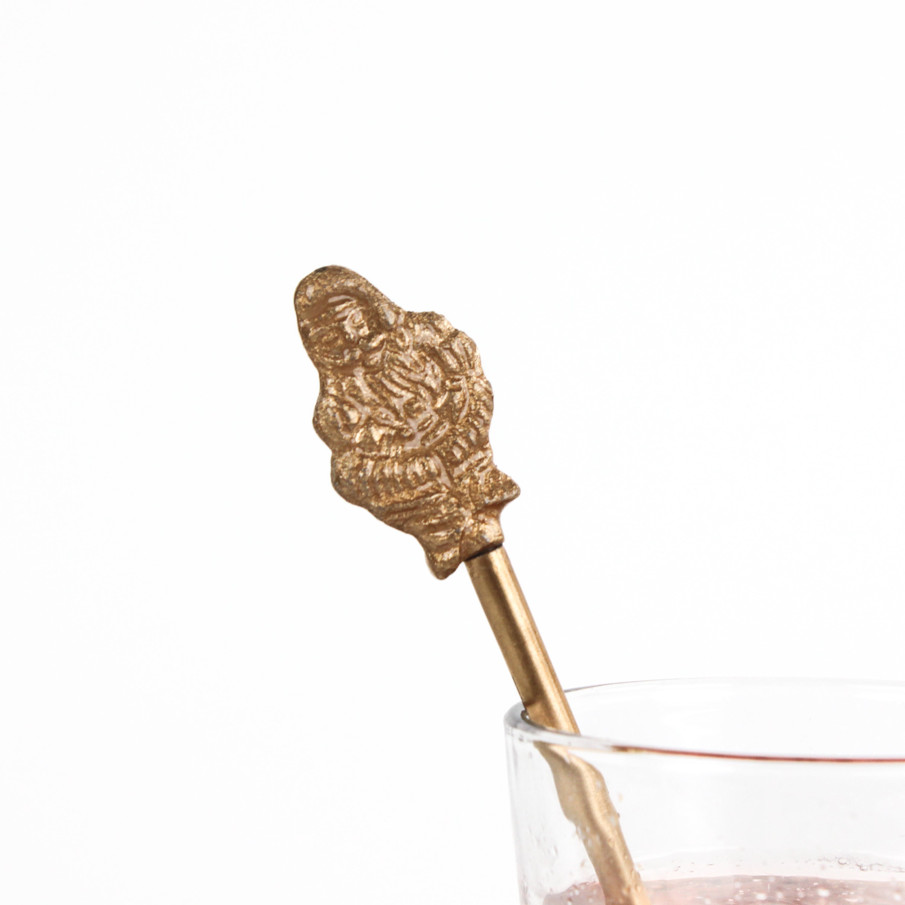 a close up of gilt metal gold christmas swizzle stick with decorative santa ends on a white background