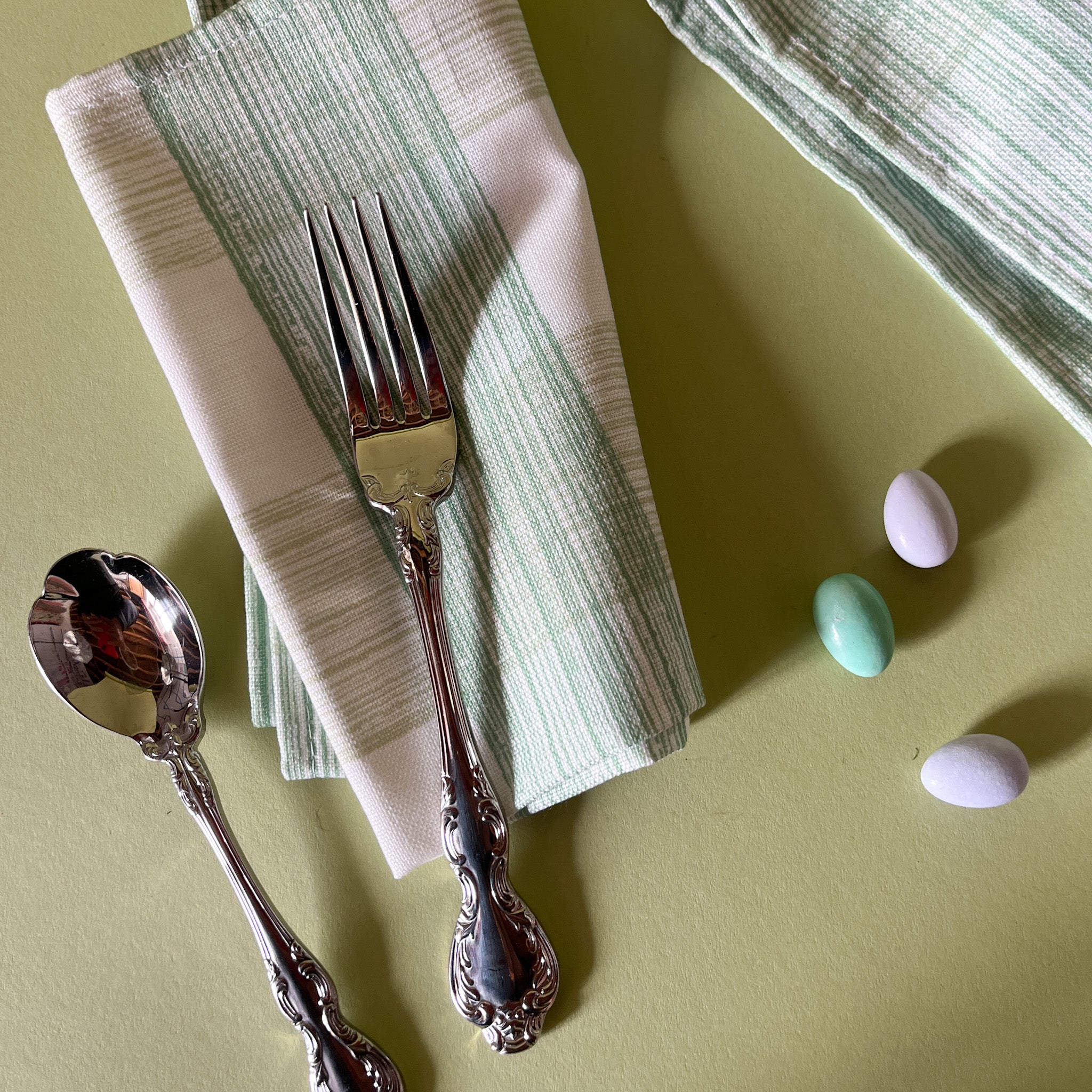 two green dinner napkins in gin lane print fabric by madap cottage next to cutlery and small easter eggs