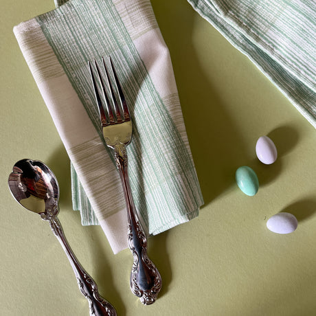 two green dinner napkins in gin lane print fabric by madap cottage next to cutlery and small easter eggs