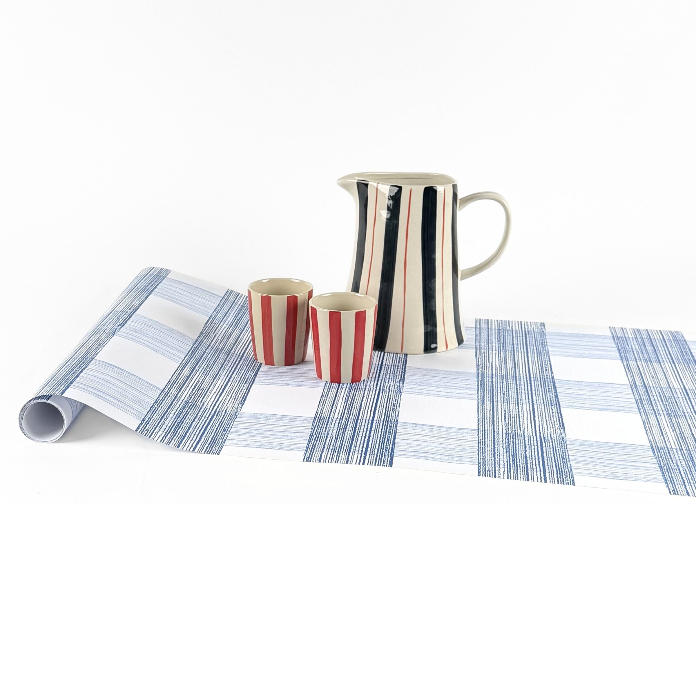 Gingham blue paper table runner styled with striped pitcher and matching cups.