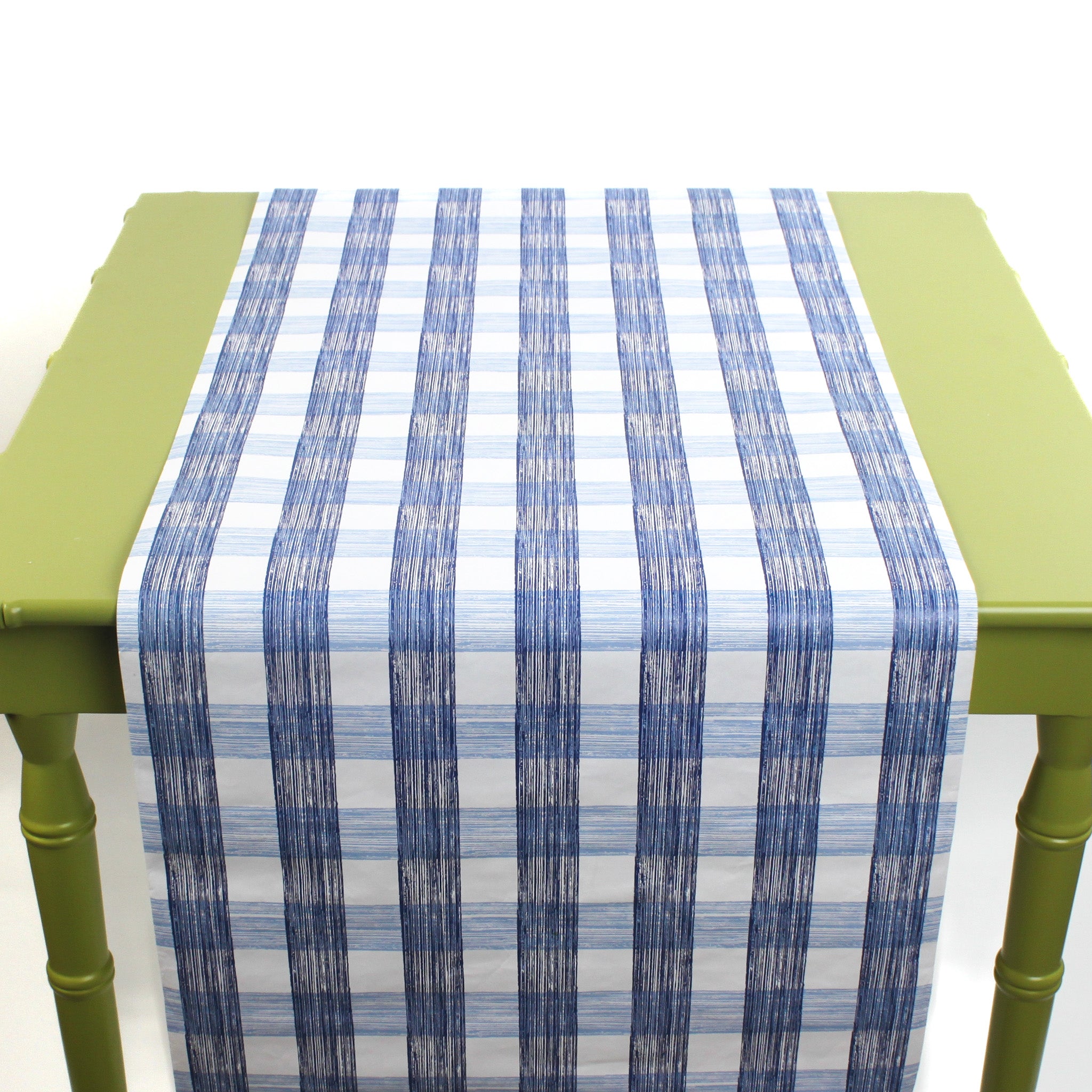 a green table covered by a Gin Lane Blue Gingham Paper Table Runner on a white background