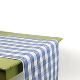 a green table covered by a Gin Lane Blue Gingham Paper Table Runner on a white background