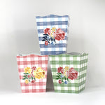 a trio of gingham with floral motif wastepaper baskets - one pink, one blue and one green. 