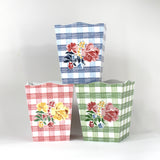 a trio of gingham with floral motif wastepaper baskets - one pink, one blue and one green. 