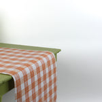 a green table covered with a gingham orange paper table runner in a pattern called gin lane by madcap cottage