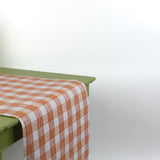 a green table covered with a gingham orange paper table runner in a pattern called gin lane by madcap cottage